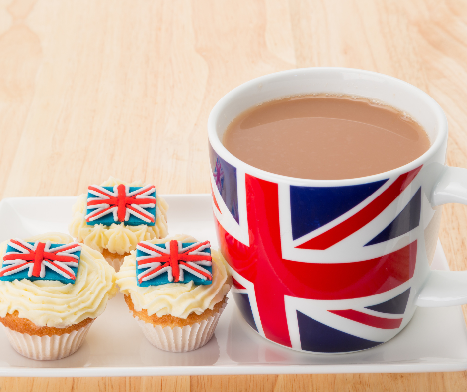 na zdjęciu jest kubek z bawarką. kubek jest z brytyjską flagą. obok leżą babeczki z brytyjską flagą